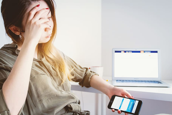 woman holding he head looking at cell phone