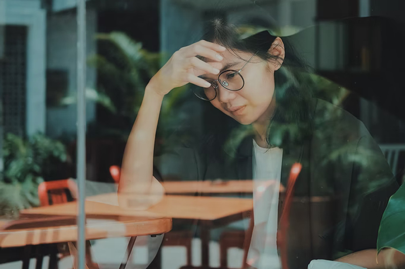 woman sitting at table with hand on forehead