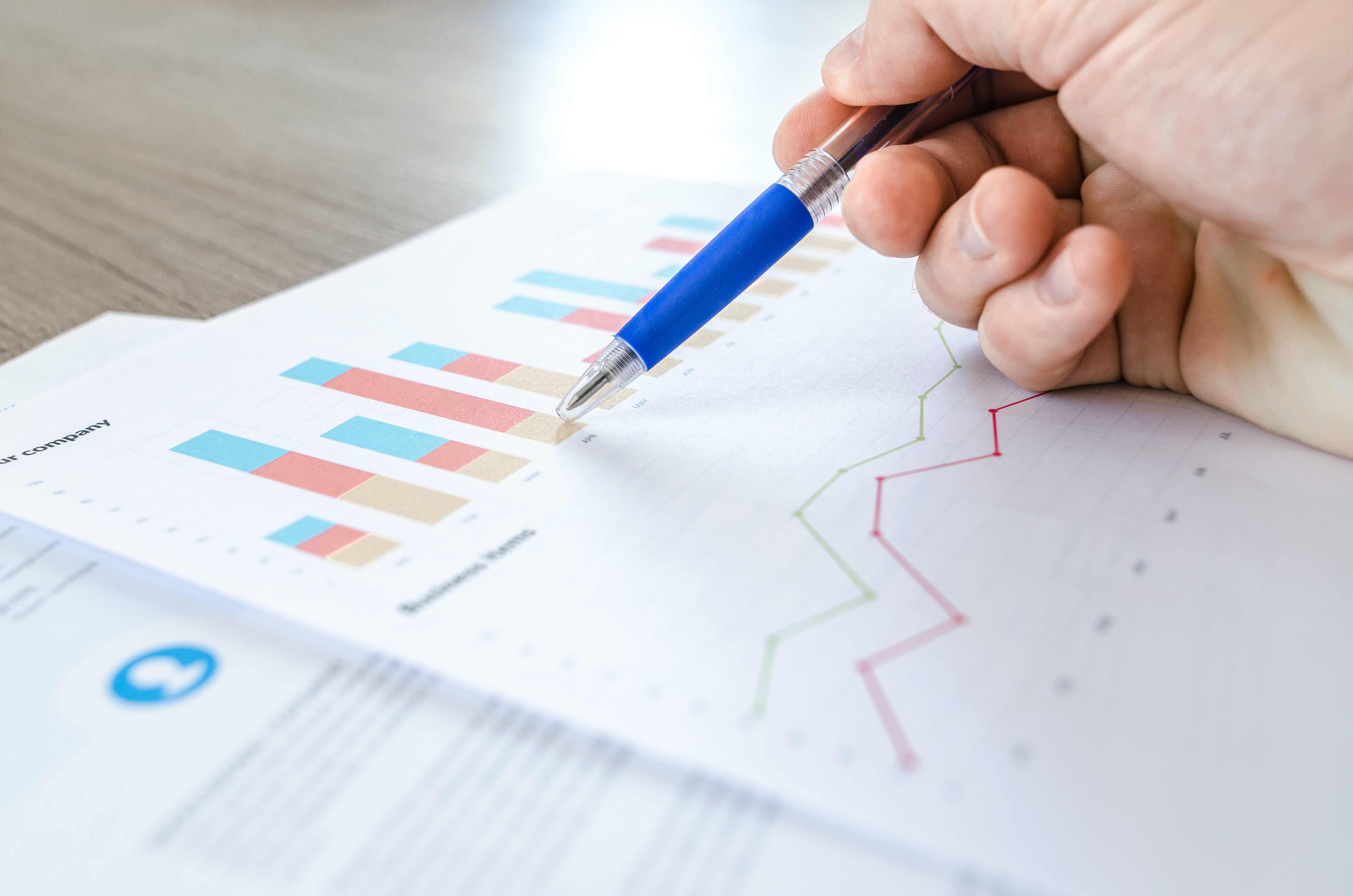 hand holding a pen, pointing at data tables on paper